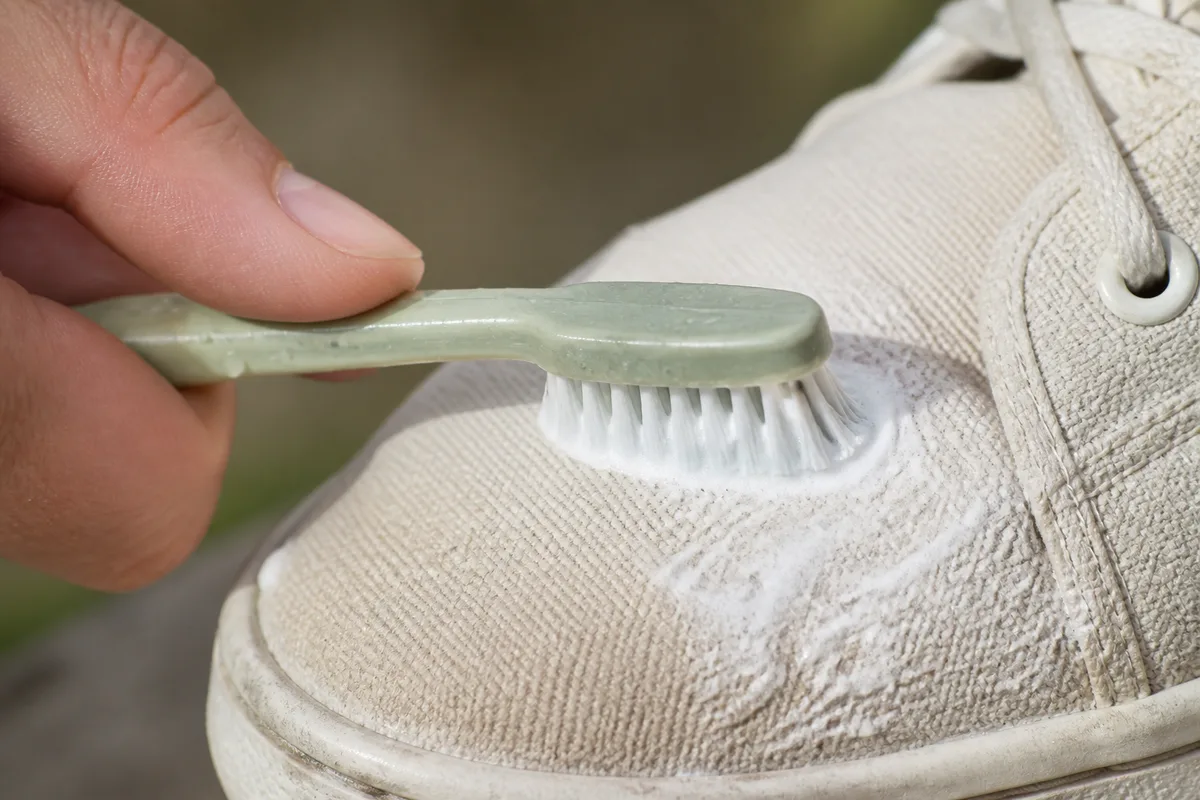 Gros plan sur une brosse à dents appliquant une pâte blanche sur la toile d&rsquo;une sneaker